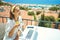 Pleased woman enjoying coffee while sitting on terrace on sea resort, using laptop computer for remote work