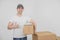 Pleased young delivery man standing near a stack of cardboard packages, giving thumb up and holding one box.