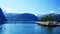 A pleasure boat is slowly leaving Valldal, Norway on the calm waters of a fjord on a sunny day with snow on the peaks.