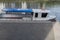 Pleasure boat with white cabin and deck with blue awning stretched on top, with railing. Life jackets on deck under seat.