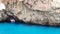 A pleasure white motor boat floats in the blue Mediterranean Sea against a background of brown rocks