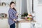 Pleasured pregnant woman holding her belly, dressed plaid shirt, curly long hairs. Female is in kitchen interior