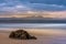 Plettenberg Bay beach at sunset, with hills in the distance and a rock in the foreground.