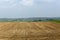 Plowed agriculture field and a village on background