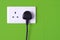 Plugged in socket against green tiles background