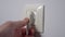 Plugging power electrical plug in electric socket on a white home wall.