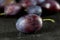 Plum on dark wood, closeup against blurred plums in the backgrou