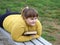 Plump girl lying on bench in park, holds book in her hands and looks away