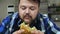 Plump guy with a beard bites a piece of hamburger. The food is very delicious. The plump guy is glad. Unhealthy