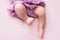 Plump legs of a newborn girl in a lilac skirt, young ballerina dancer, fingers on her feet, dance moves, pink background,