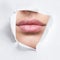 Plump lips peep into the slit of white paper