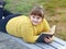 Plump smiling girl lying on bench in park, holds book in her hands and looks away