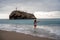 A plump woman in a bathing suit enters the water during the surf. Alone on the beach, Gray sky in the clouds, swimming