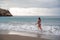 A plump woman in a bathing suit enters the water during the surf. Alone on the beach, Gray sky in the clouds, swimming