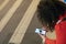 A plump woman with long curly dark hair in a bright red suit with a phone in her hands is sitting in the center of a European city