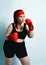 Plump young girl in black sporty top, shorts and red boxing gloves looks up thinking over strategy in forthcoming fight.