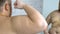 Plump young man looking at biceps reflection in mirror, posing at home, fitness