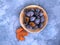 Plums in a bamboo bowl and a dry autumn leaf on a blue background