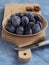 Plums in a bamboo bowl, slit plum and a knife on a bright wooden board and a blue background