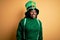 Plus size african american woman with braids wearing green hat with clover on st patricks day looking away to side with smile on