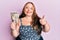 Plus size caucasian young woman holding japanese yen banknotes smiling happy and positive, thumb up doing excellent and approval