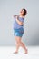 Plus size fashion model in jean shorts, fat woman on gray background