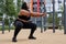 Plus size fat afro american woman squats in sports ground. Weight losing, obesity