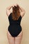Plus Size Model. Woman From Back Portrait. Full-figured Brunette In Back Bodysuit Keeping Hands On Head And Touching Hair.