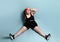 Plus size redhead female in red headband, black top, shorts, sneakers. Sitting on floor, legs wide apart, tired. Blue background