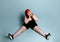 Plus size redhead lady in red headband, black top, shorts, sneakers. Sitting on floor, legs wide apart, surprised. Blue background