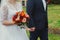 Plus size wedding couple is walking outside. Curvy bride is holding beautiful colorful bouquet with orange, red and pink peonies