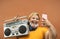 Plus size woman listening to music with vintage boombox stereo while taking selfie with mobile smartphone during corona virus