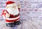 Plush Santa Claus stands on the wooden floor against the background of a red brick wall