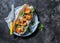 Po` boy sandwich with crispy cornmeal shrimp, tomatoes, cilantro and mayo herbs sauce on dark background, top view