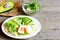 Poached egg, avocado slices, salad mix, sauce, spices in a tortilla. Avocado half on a wooden board, salad mix in a glass bowl