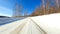 Point of view: driving on country snow-covered track along the trees in the morning sunny time