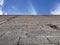 Point of view looking at the blue sky with few clouds, at the base of the image a gray wall of rustic construction blocks