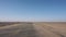 The point of view of someone driving a vehicle on the empty desert road, sands moving through the road by wind.