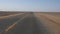 The point of view of someone driving a vehicle on the empty desert road, sands moving through the road by wind, looks like waves