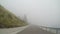 Point of view of vehicle driving in bad weather and poor visibility through thick fog on mountain road -