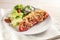 Pointed bell pepper baked with rice, tuna, tomatoes and cheese, lettuce salad, and dip, on a white plate and napkin, bright wooden