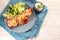 Pointed bell pepper stuffed with rice, tuna, tomatoes and cheese on a blue plate with lettuce salad, and dip, on a napkin and a