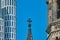 Pointed tower with cross of the memorial church in front of a blue sky next to a modern high-rise building with strict rectangular