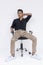 A poised young Filipino man is seated comfortably in an office chair against a white background, exuding confidence
