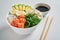 poke bowl with salmon, avocado, rice, Chuka Salad, sweet onions, quail eggs sprinkled with white and black sesame with chopsticks