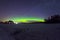 Polar northen lights aurora borealis at night in the starry sky above the lake with the island and the silhouette of the trees by