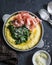 Polenta with butter stewed spinach and prosciutto in a frying pan. Delicious lunch in a mediterranean style. On a dark background