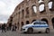A police car is on duty near the wall of the amphitheater Colosseum construction years 72-80, monuments of Ancient Rome.