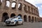 A police car stands in front of the amphitheater Colosseum, monuments of Ancient Rome.