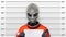 Police-style mugshot of an alien character dressed in an orange spacesuit, holding an empty name placard against height chart